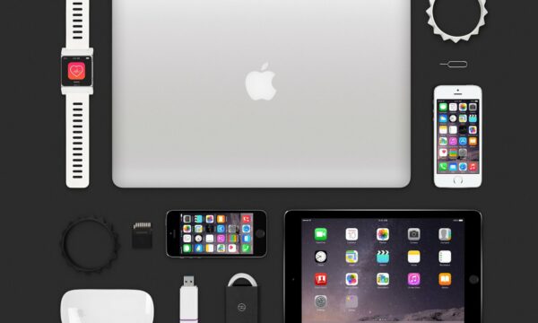 Various Apple devices and accessories arranged on a black surface, including a MacBook, iPhone, iPad, smartwatch, USB drive, and charging cables.