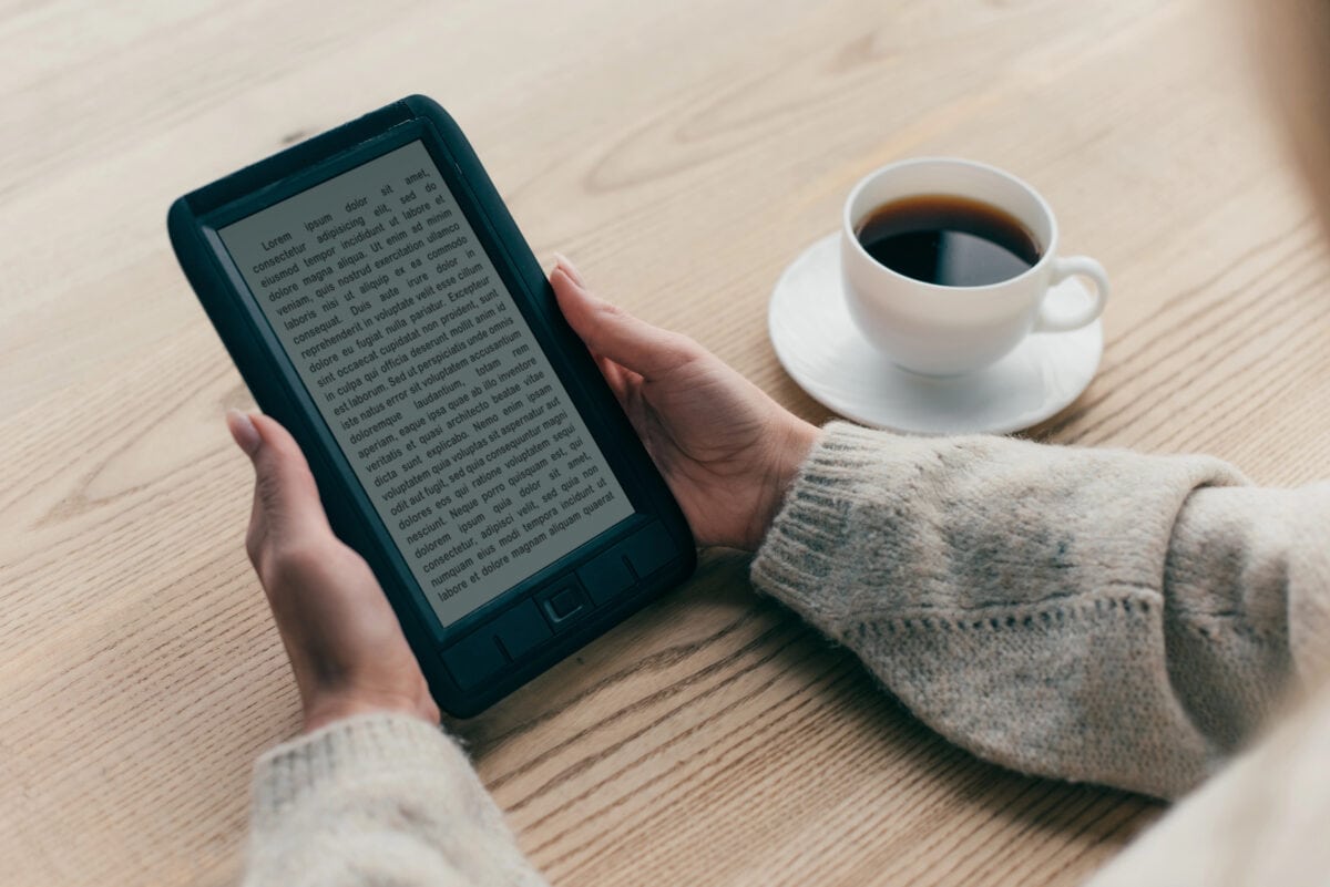 Cropped view of woman studing with e-book near cup of coffee