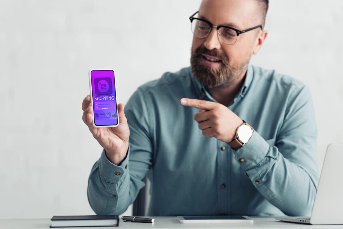 Handsome man in shirt pointing with finger at smartphone with shopping website