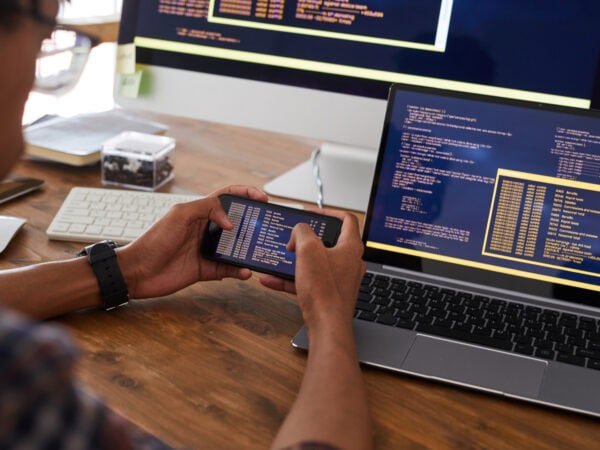 Close up of male hands holding smartphone with code on screen while working at desk in office, IT developer concept, copy space