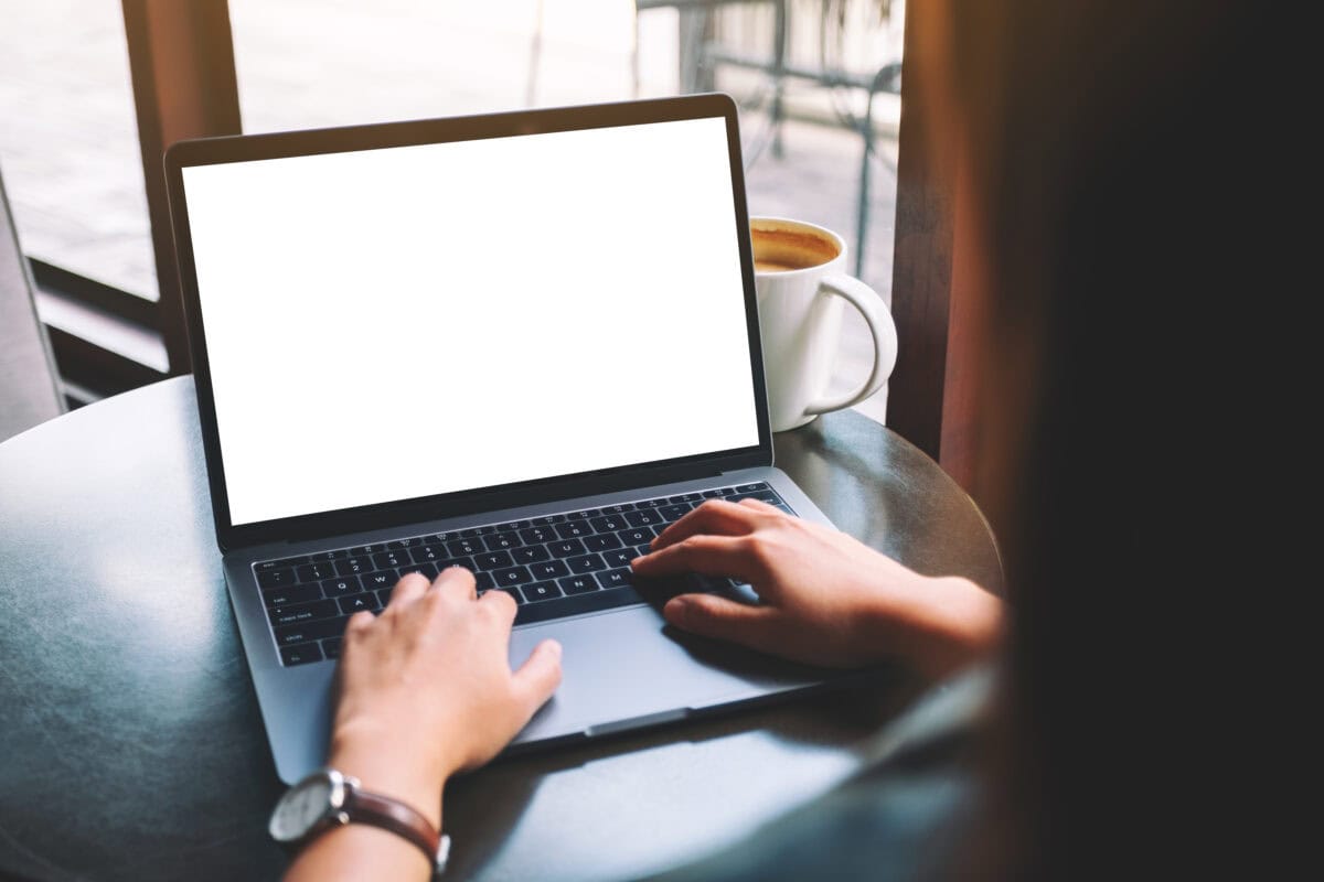 Mockup image of a woman using and typing on laptop with blank white desktop screen with coffee cup on the table