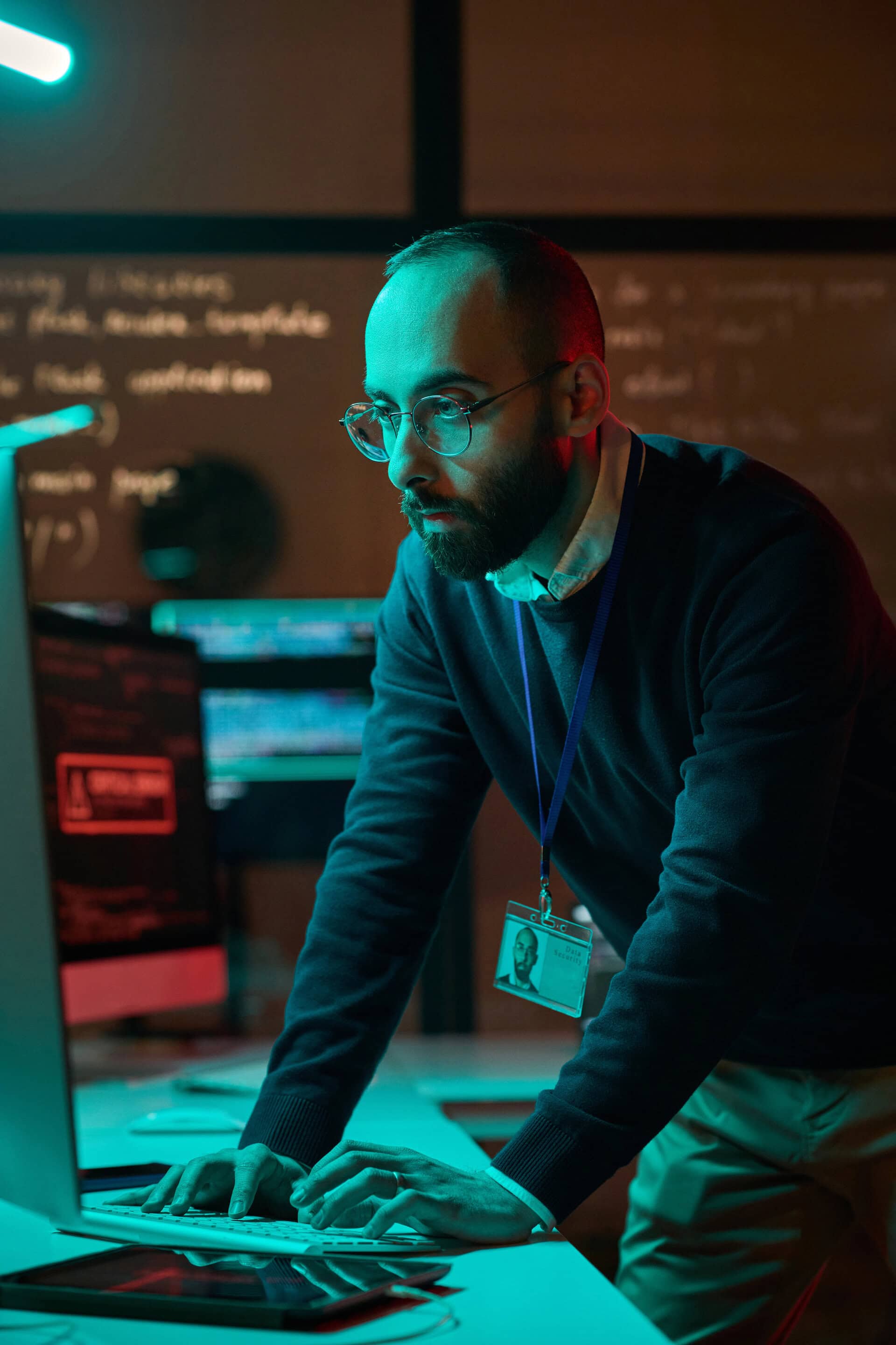 Vertical portrait of bearded cybersecurity engineer working with computer network in blue neon lights