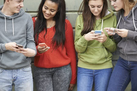 Four people stand side by side, wearing casual clothes and using smartphones.