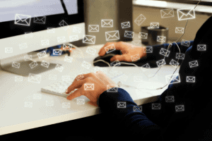 Person typing on a keyboard at a desk, with illustrated envelope icons symbolizing emails floating around.